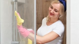 White vinegar, spray bottle, microfibre cloth and soft sponge arranged beside a shower screen.