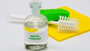 White vinegar, spray bottle, microfibre cloth and soft sponge arranged beside a shower screen.